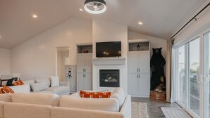 A modern living room with a fireplace, white furniture, and a large window. - Mountain View Lodge - Spacious Cabin Retreat with Hot Tub, (Scofield)