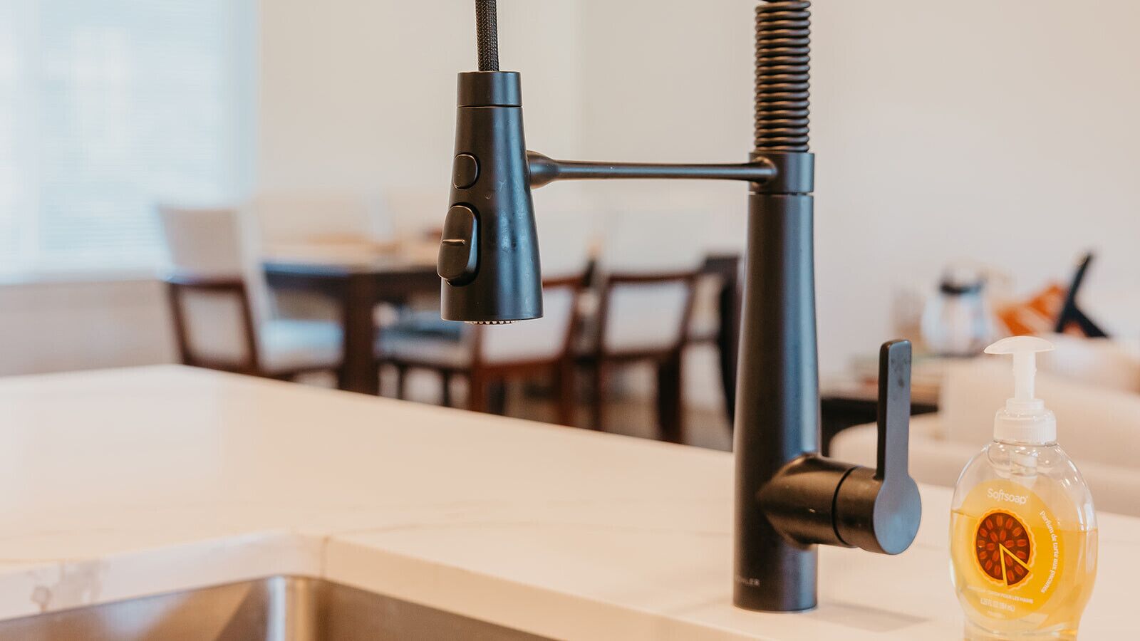 Une cuisine moderne avec un robinet élégant, un flacon de savon et, au fond, un coin repas.