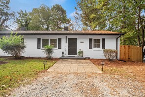 A single-story white house with a dark brown door, a small porch, and a wooden fence. - 5 Min to Downtown - Desk  - Fenced Yard - Wi-Fi (Raleigh)