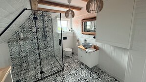 A bathroom with a patterned floor, a glass shower enclosure, a sink with a bowl, and a wooden ceiling beam.