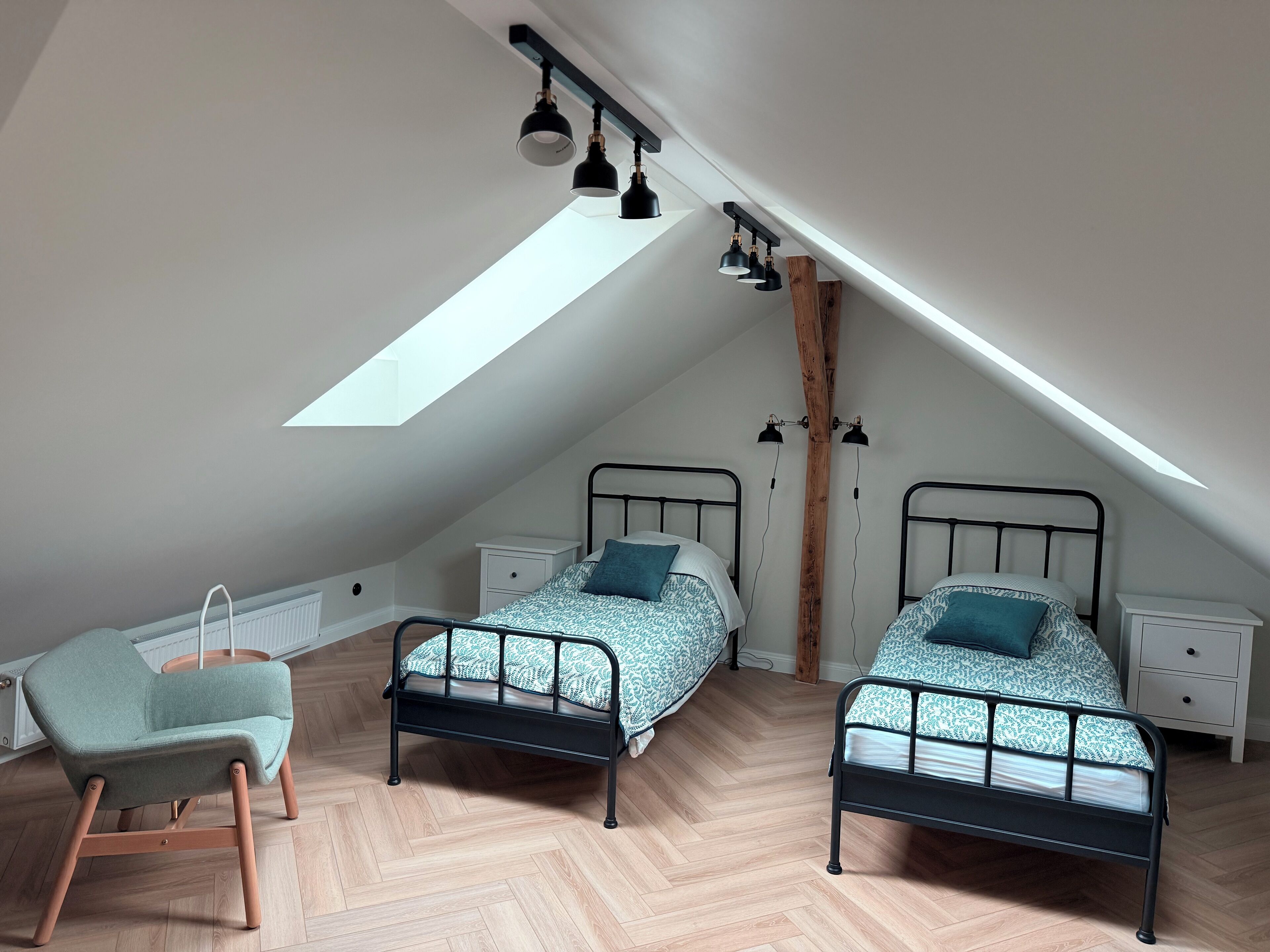 Een slaapkamer in loftstijl met twee bedden, een stoel en een dakraam.