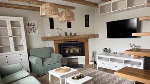 A living room with a sofa, a green armchair, a coffee table, a fireplace, a TV, and a cabinet.