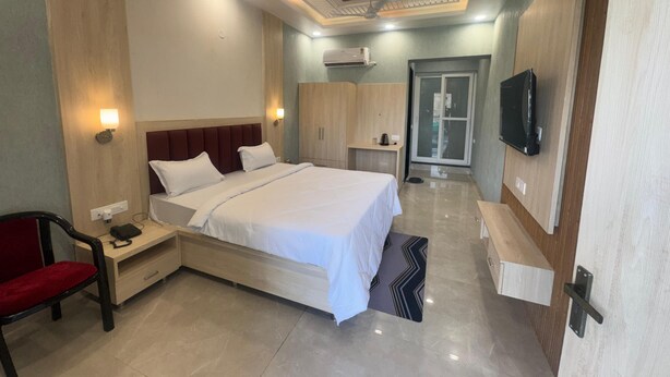 A hotel room with a large bed, bedside tables, a chair, a TV, and a wardrobe. - KANHA RETREAT - VRINDAVAN (Vrindavan)