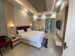 A hotel room with a large bed, bedside tables, a chair, a TV, and a wardrobe. - KANHA RETREAT - VRINDAVAN (Vrindavan)