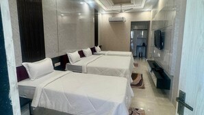 A hotel room with two beds, a ceiling fan, recessed lighting, an air conditioning unit, a television, and a bathroom visible in the background. - KANHA RETREAT - VRINDAVAN (Vrindavan)