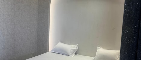 A modern hotel room with a curved ceiling, a single bed with white bedding, a red chair, and a blue mat labeled "BATHROOM".