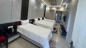 A hotel room with two beds, a desk, a chair, a TV, and a minibar. - KANHA RETREAT - VRINDAVAN (Vrindavan)