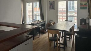 A modern kitchen with a wooden countertop, a dining table with chairs, and a view of buildings through large windows. - Balcony Apartment on Canal Saint Martin (Paris)