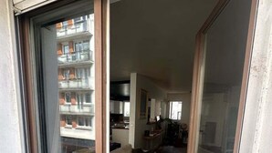 A modern apartment with a sliding glass door leading to a living area with a sofa and a dining table. - Balcony Apartment on Canal Saint Martin (Paris)