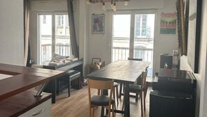 A compact kitchen with a dining area, wooden flooring, and a black refrigerator. - Balcony Apartment on Canal Saint Martin (Paris)