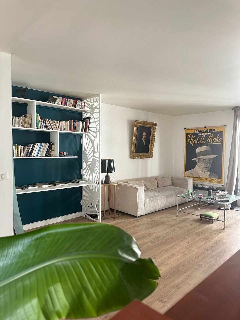 Un salon avec une bibliothèque, un canapé, une table basse et une affiche accrochée au mur.