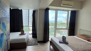 A hotel room with two beds, large windows, a ceiling fan, and an air conditioning unit.