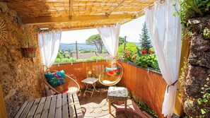 A covered patio with wicker furniture, a small table, and a view of a garden with flowers and trees. - Moulin Lombard B&B (Les Arcs-sur-Argens)