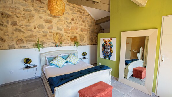 A bedroom with a stone wall, a bed with patterned pillows, a bedside lamp, and a mirror. - Moulin Lombard B&B (Les Arcs-sur-Argens)