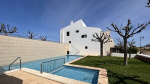 A modern building with a swimming pool, a white exterior, and a clear blue sky. - Large house with shared pool near the sea (Fornells)