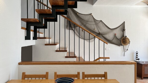 A staircase with wooden steps and black railings, a dining table with chairs, and a decorative net hanging from the railing. - Large house with shared pool near the sea (Fornells)