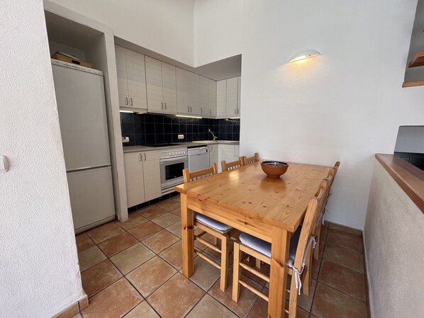 A compact kitchen with white cabinets, a wooden dining table, and a tiled floor. - Large house with shared pool near the sea (Fornells)