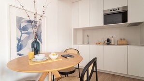 A modern kitchen with white cabinets, a built-in oven, and a dining area with a round wooden table and wicker chairs.