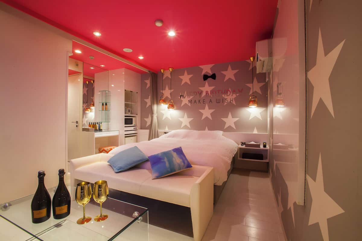 Une chambre à coucher moderne avec un lit, des tables de chevet et un meuble vitré contenant des bouteilles et des verres.
