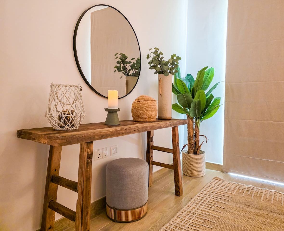 A wooden console table with a mirror, candle, and potted plants.