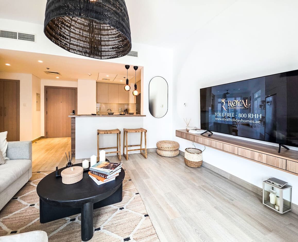 A modern living room with a sofa, coffee table, and TV. There's a kitchen area in the background.
