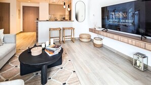 Una sala de estar moderna con un sofá, una mesa de centro y un televisor. Se observa un área de cocina al fondo.