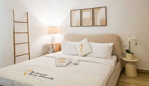 A neatly arranged bedroom with a bed, pillows, a bedside table with a lamp, a wall-mounted artwork, a ladder, and a small potted plant. - Modern 1BR Apartment near Yas Mall & Ferrari World (Abu Dhabi)