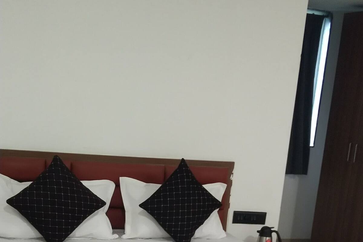 A neatly made bed with a white mattress and dark bedding, a wooden headboard, and two black pillows with a grid pattern.