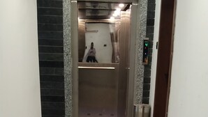 A hallway with a shiny tiled floor leading to an elevator. - Hotel Joy Executive  (Pune)