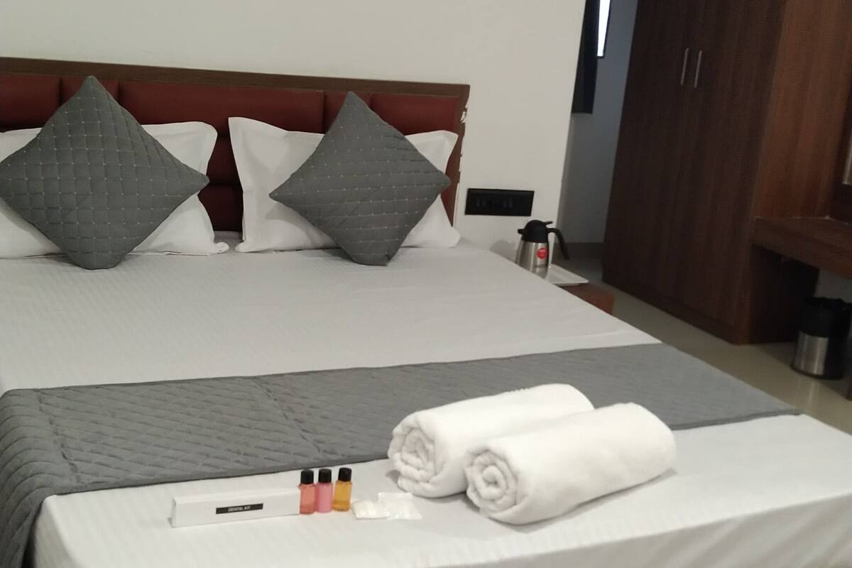 A neatly made bed with pillows, a bedside table with a coffee maker, and a wooden wardrobe.