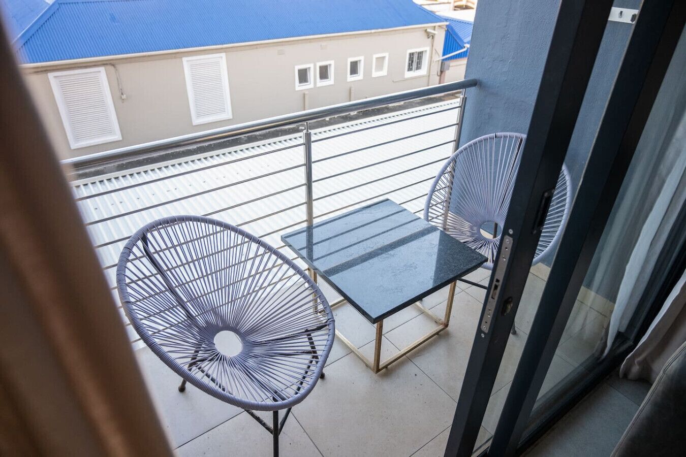 A balcony with two chairs and a table, overlooking a residential area with houses.