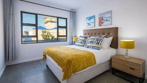 Hotelkamer met een groot bed, nachtkastje met een lamp en een raam met uitzicht op gebouwen en een toren.