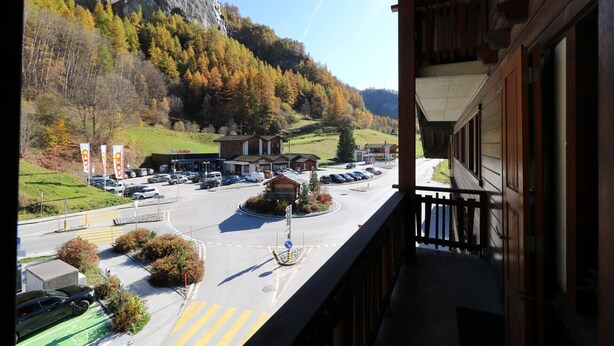 Vista de un estacionamiento con coches, un edificio con un rótulo y una montaña al fondo.