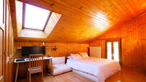 Acogedora habitación tipo cabaña de madera con cama, escritorio y ordenador, y un tragaluz.