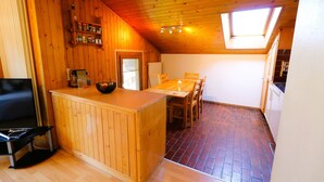 Una habitación acogedora, con muebles de madera, una mesa de comedor, sillas, una pequeña cocina y una estantería empotrada con frascos.