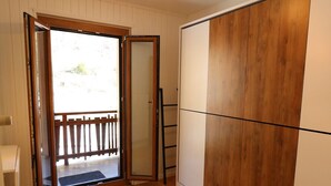 Una habitación con suelo de madera, una puerta corredera que da a un balcón exterior y un armario con acabado de madera.