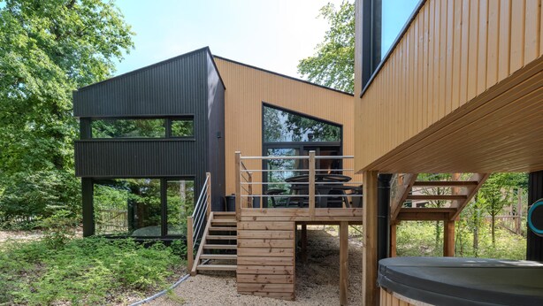 A modern outdoor living area with a hot tub, wooden deck, and a staircase leading to a deck with outdoor furniture. - Design house with wellness in nature (Biron)