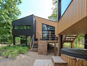 A modern outdoor living area with a hot tub, wooden deck, and a staircase leading to a deck with outdoor furniture. - Design house with wellness in nature (Biron)