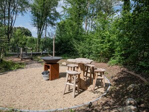 An outdoor seating area with a stone table and wooden stools, surrounded by gravel and trees. - Design house with wellness in nature (Biron)