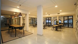 A spacious, modern dining area with multiple tables and chairs, large windows, and a clean, minimalist design.