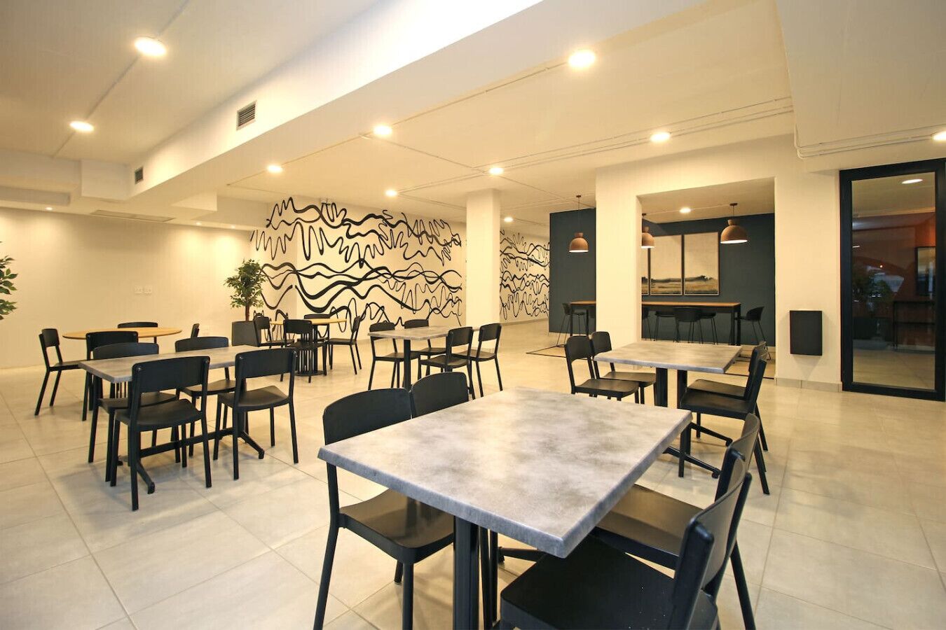 A modern dining area with multiple tables and chairs, a decorative wall, and a large window.