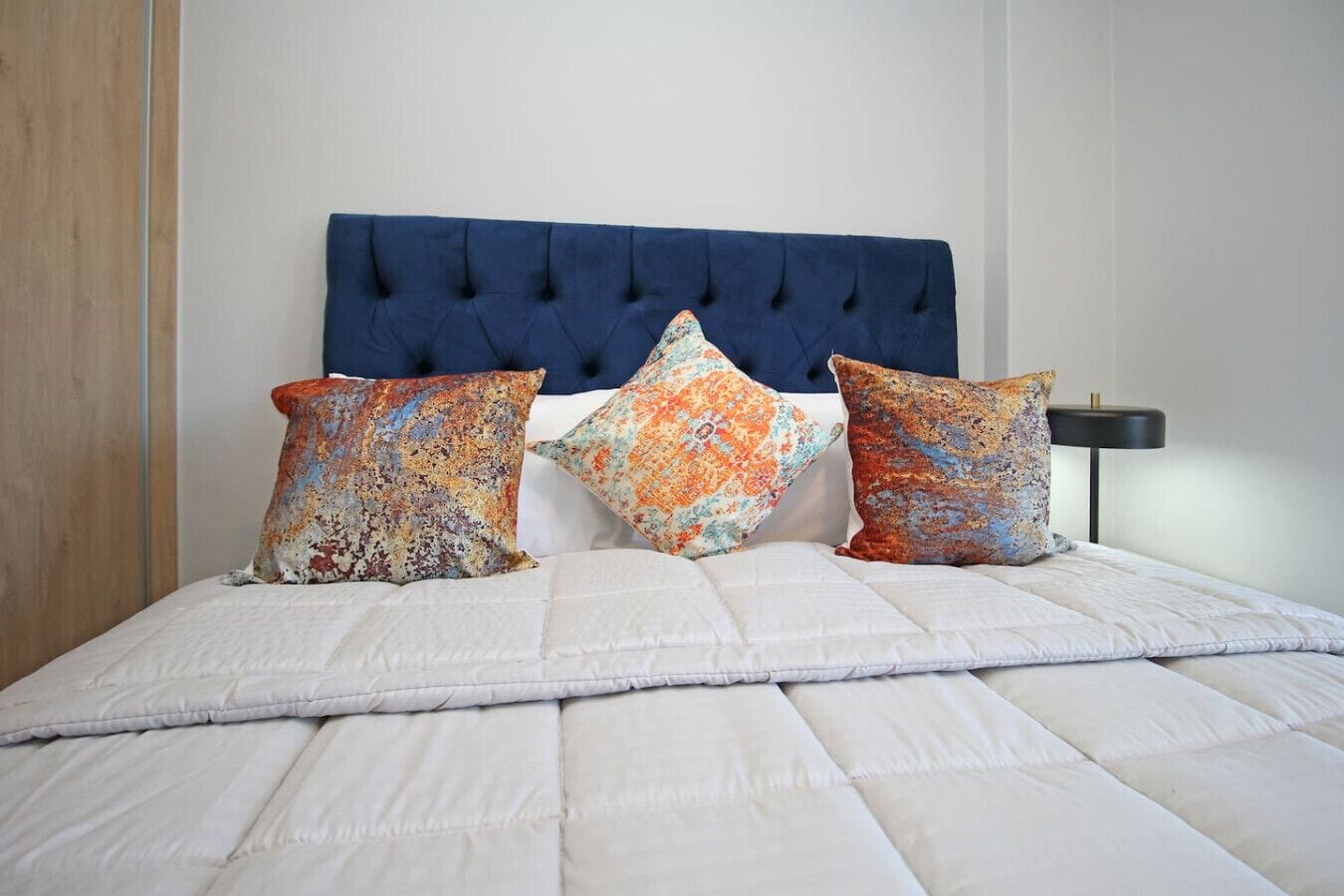 Een bed met een gestoffeerd hoofdbord en drie gekleurde kussens.
