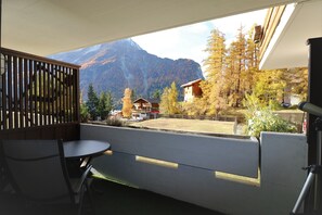 Un balcón con vistas a una montaña, una cerca de madera y una mesa con sillas.