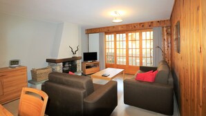 A cozy living room with a fireplace, wooden walls, a television, and a large window. - Veisivis 74  Tout confort  piscine  La Forclaz (La Forclaz)