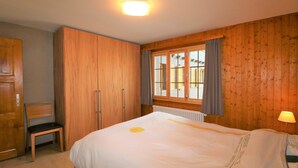 A bedroom with wooden walls, a bed, a chair, and a window with curtains. - Veisivis 74  Tout confort  piscine  La Forclaz (La Forclaz)