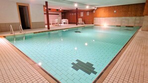 A rectangular indoor swimming pool with tiled floors and walls, surrounded by wooden paneling and a few white chairs. - Veisivis 74  Tout confort  piscine  La Forclaz (La Forclaz)