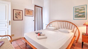 A bedroom with a wooden bed, a nightstand, a lamp, and two framed artworks on the wall. - Hanbury Apt Pool And Sea (Ventimiglia)