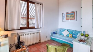 A room with a window, a radiator, a sofa, a wicker chair, and a wall-mounted picture. - Hanbury Apt Pool And Sea (Ventimiglia)