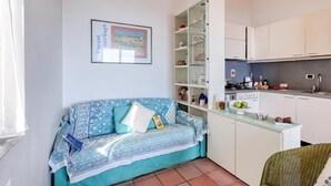 A compact living space with a sofa, a glass cabinet, a kitchen area, and a framed picture on the wall. - Hanbury Apt Pool And Sea (Ventimiglia)