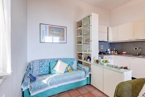 A compact living space with a sofa, a glass cabinet, a kitchen area, and a framed picture on the wall. - Hanbury Apt Pool And Sea (Ventimiglia)